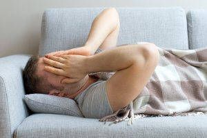 man laying down on couch with face over hands