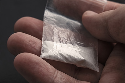 La mano dell'uomo che tiene sul palmo un pacchetto di plastica con polvere di cocaina o un'altra droga.