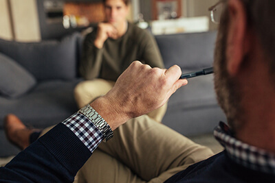 Hands of psychologist holding a pen and listening to man during therapy session.